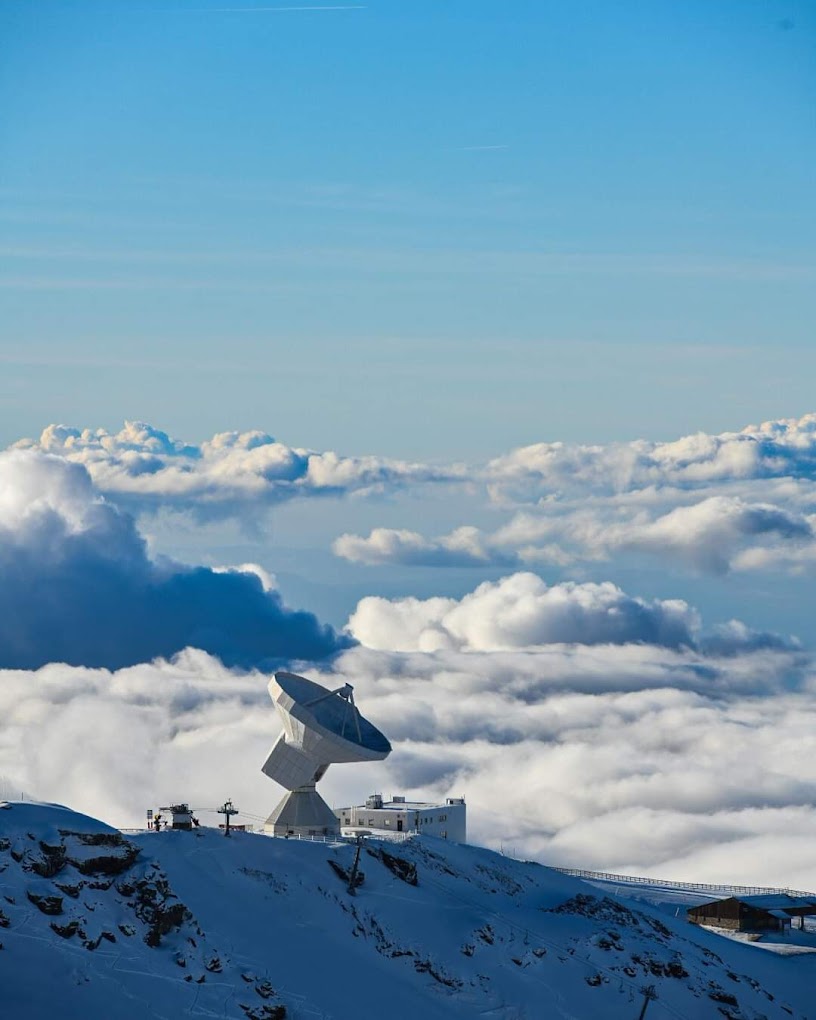 A breathtaking winter view of Sierra Nevada in Spain featuring a sprawling snow-covered mountain under a clear sky. The scene is enriched by a chalet and sports enthusiasts enjoying the winter activities.