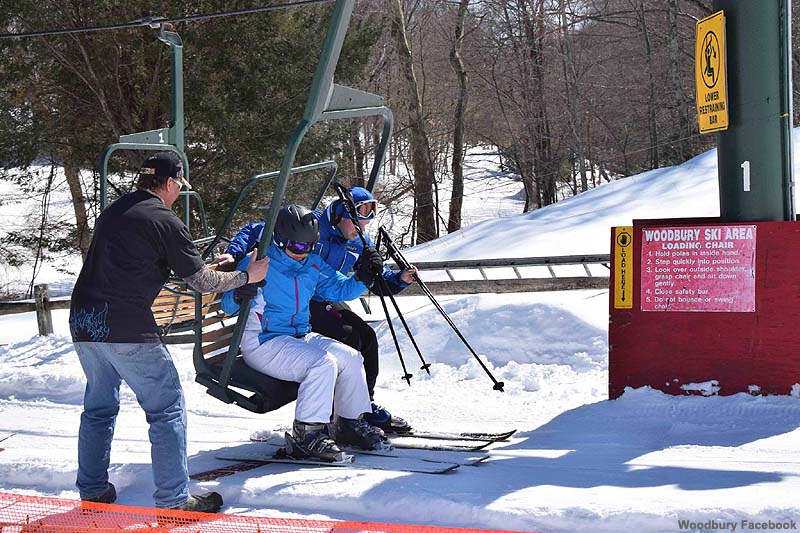 A skier is enjoying the winter sports scene on the slopes of Woodbury Connecticut. The ski lift in the background suggests a ski resort setting. A family can be seen skiing in the far distance.