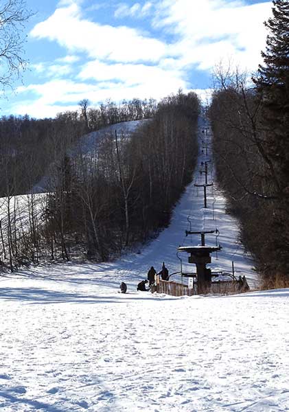 Winter scene at Duck Mountain – Kamsack, Saskatchewan, Canada, showing a bustling ski resort with a ski lift in operation, skiers enjoying the white, snow-covered slopes.