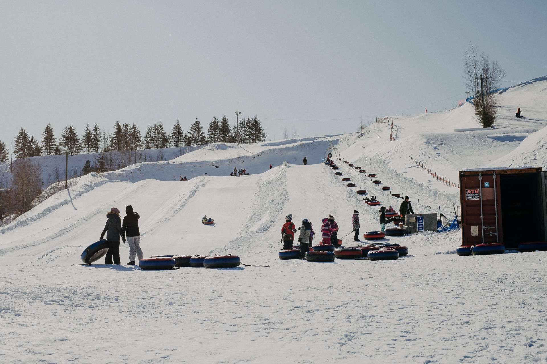 A winter sports scene at Beauce – Vallée-Jonction Quebec featuring a bustling winter sports centre and popular ski resort. Snow-covered slopes and a glimpse of a snowmobile can also be seen.