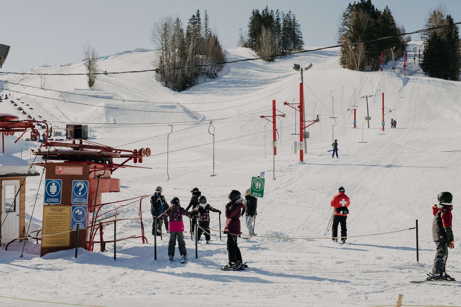 A captivating winter sports scene at Beauce – Vallée-Jonction in Quebec highlighted by a ski lift working amidst a bustling ski resort. A solitary skier adds life to the frosty panorama.