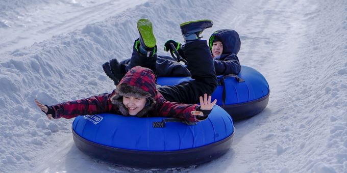 Enjoy a thrilling winter sports scene at The Rock Snowpark in None Wisconsin featuring a snowmobile zipping past a cozy chalet amidst a picturesque winter landscape.