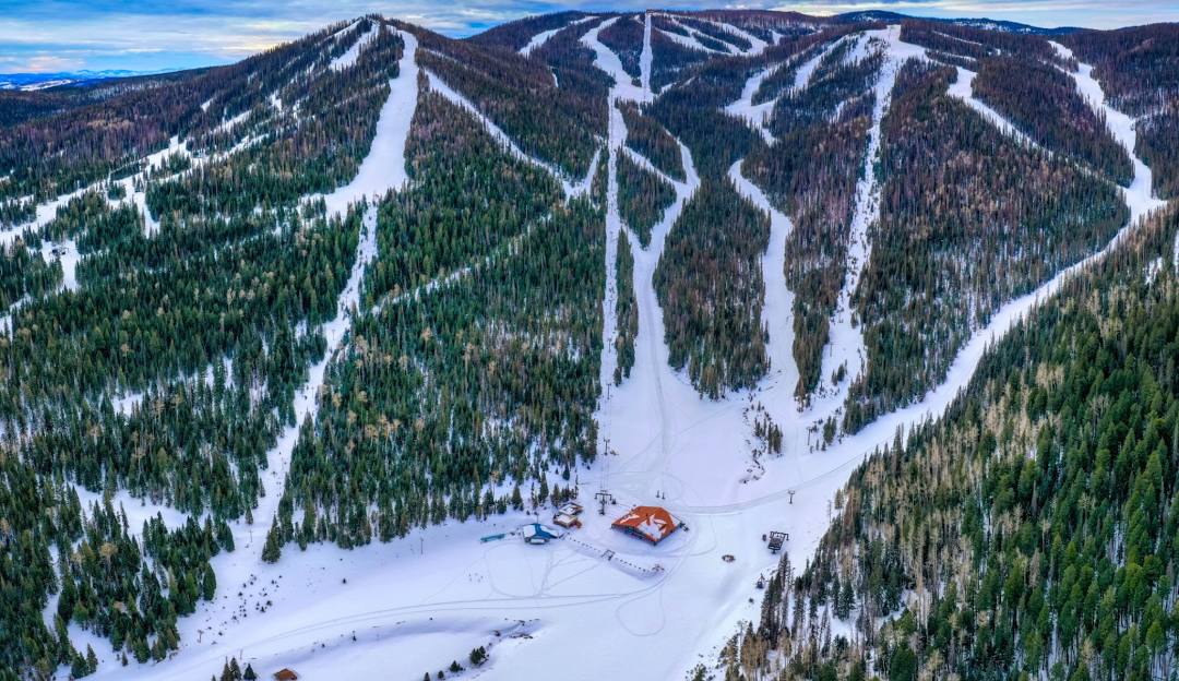 A ski resort in Arizona's Sunrise Park, featuring a ski lift ascending snow-covered slopes, creating a picturesque winter sports scene. A skier dots the landscape, enjoying the crisp weather.