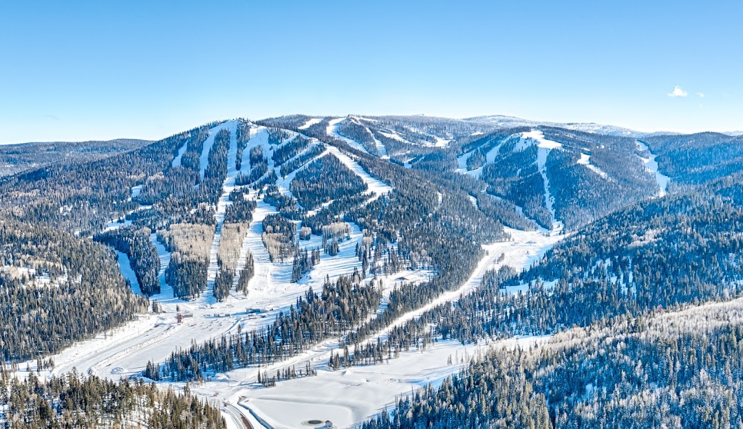 A vibrant view of Sunrise Park ski resort in Arizona; snow-covered slopes glisten under the sunlight. Skiers enjoy winter sports gliding down the hill and taking a ski lift up.