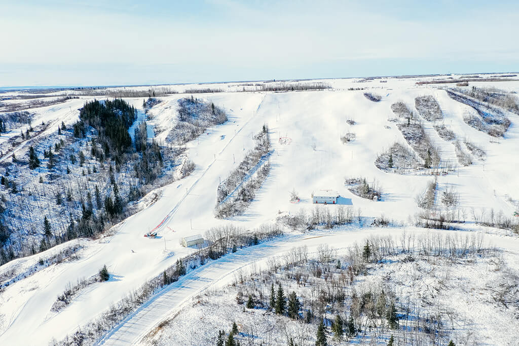 Winter scene at Fairview Ski Hill in Northern Alberta, Canada featuring a bustling ski resort, visible ski trails on snow-covered slopes, and the striking beauty of a winter sports centre.