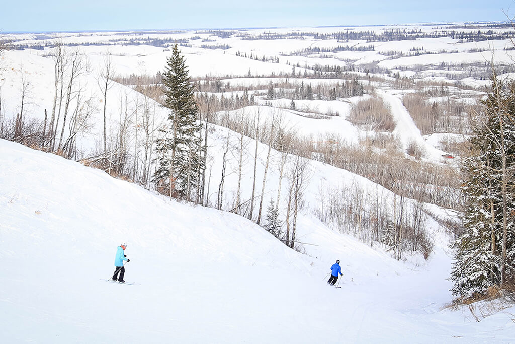Skier carving down a slope at Fairview Ski Hill in Northern Alberta, Canada; a picturesque winter scene showcasing a busy winter sports resort.