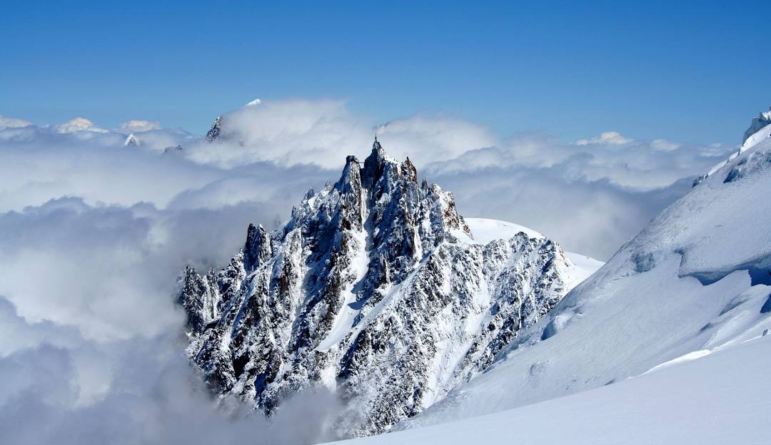 L'Aiguille du Midi in France - a snow covered mountain peak rises above the clouds.