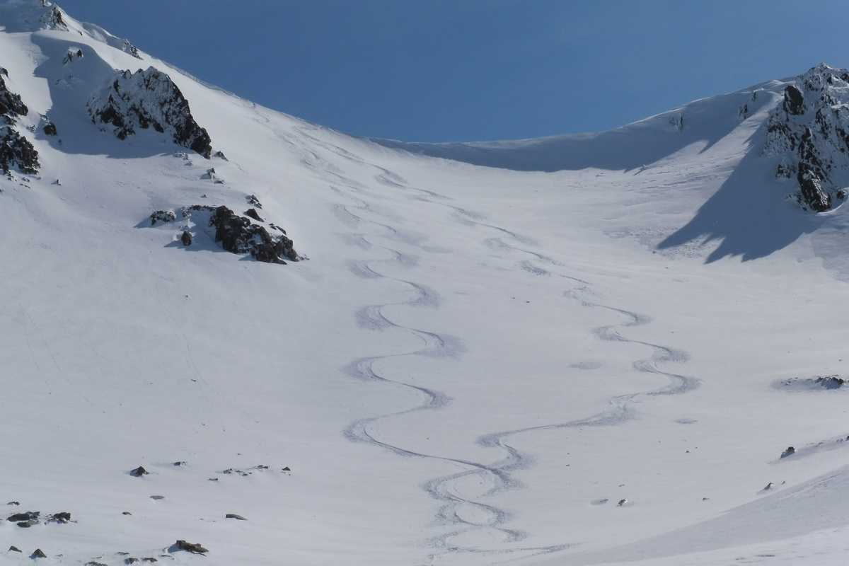 A skier enjoying a sunny winter day at a chalet in Awakino, Canterbury, New Zealand. The rugged, snow-covered mountain slopes create a stunning backdrop.