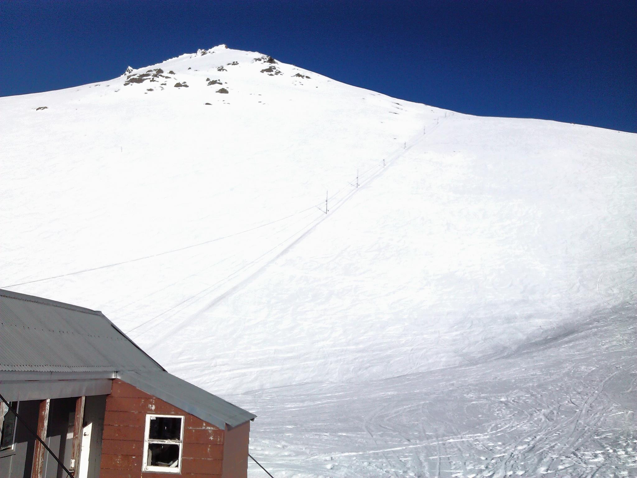 Scenic view of a chalet at the snowy Awakino ski resort in Canterbury, New Zealand, surrounded by a winter sports centre and a mountain hut, set against a stunning mountain backdrop.