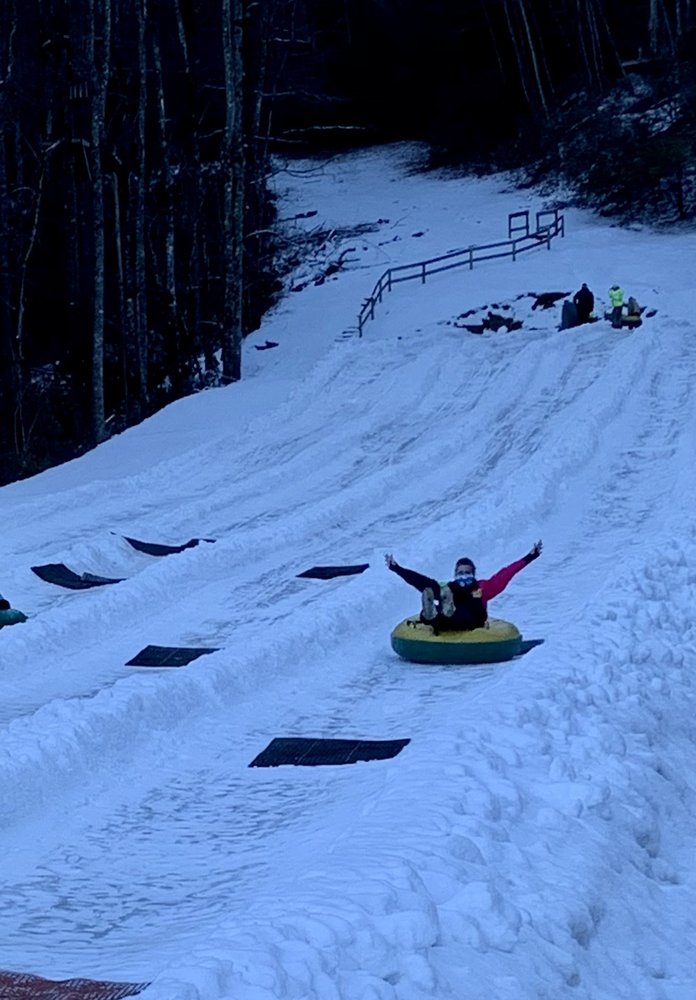 A snowmobile is the main focus in this winter scene at Sapphire Valley North Carolina. Skiers can be seen in the background near a ski lift and chalet enjoying the snowy slopes.