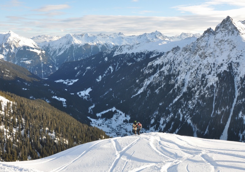 Winter view of Gargellen ski resort in Bludenz, Vorarlberg, Austria. Scene captures a skier gliding down the mountain slopes, with a chalet in the backdrop amidst snow-covered trees.