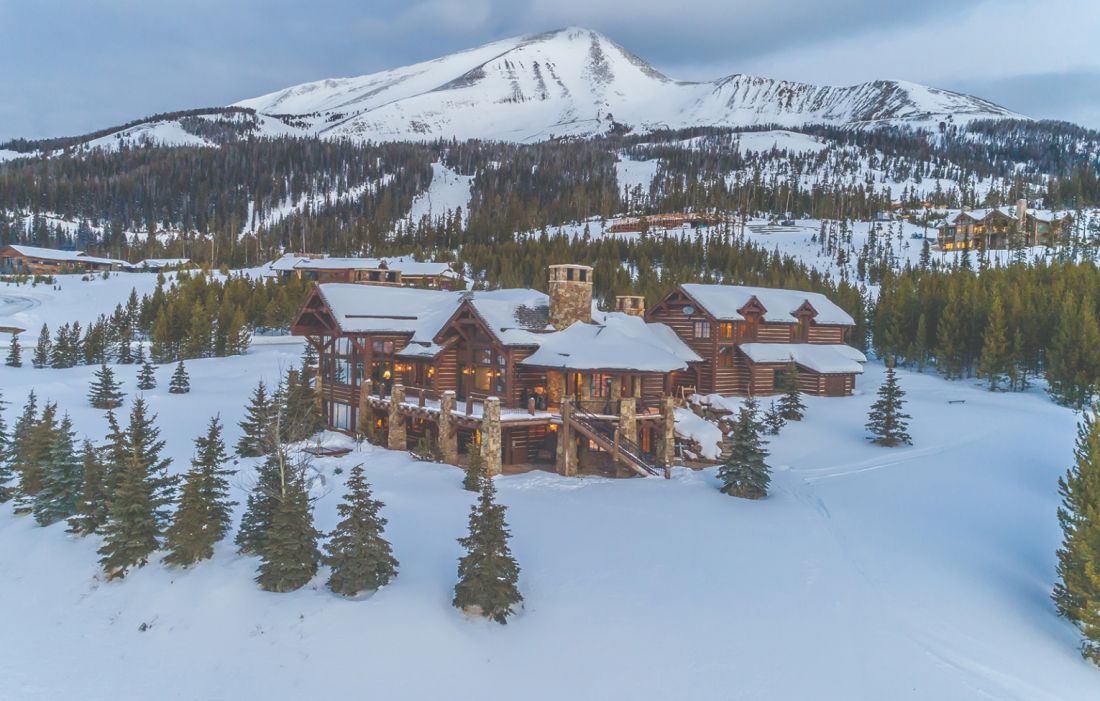 View of the Yellowstone Club in Big Sky, Montana featuring a lively ski resort surrounded by towering mountains, with a cozy lodge nestled amongst a beautiful winter landscape.