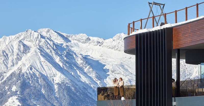A bustling ski resort at Meran 2000 in South Tyrol, Italy featuring a chalet nestled in a snowy mountain landscape, alive with winter sports activity.