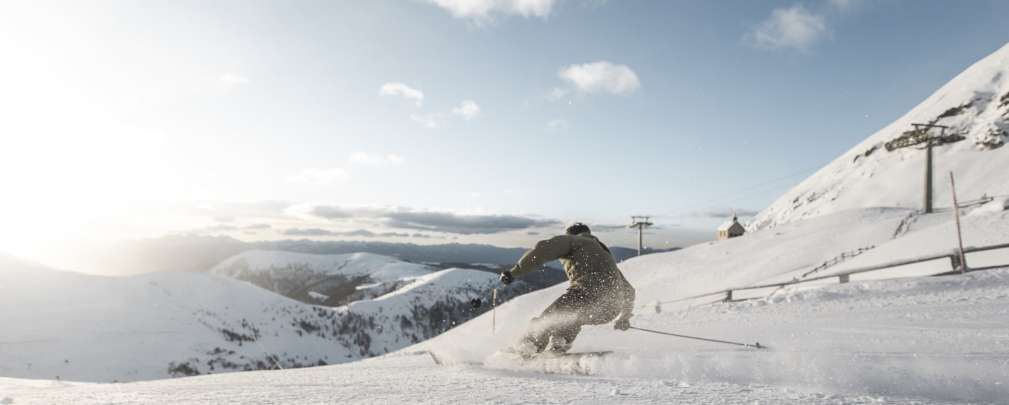 A skier and a snowboarder enjoying winter sports at the Meran 2000 resort in South Tyrol, Italy, surrounded by snow-covered slopes and a serene winter backdrop.