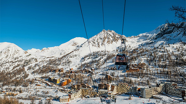 Image of a busy ski resort in Isola 2000, France showcasing a charming chalet, active ski lift, winter sports enthusiasts enjoying the snow-covered slopes.