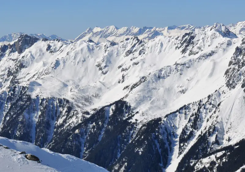 View of a charming chalet by the mountainside at the Brévent Flégère ski resort in Savoie Mont Blanc, France, with a visible skier enjoying a thrilling ride.