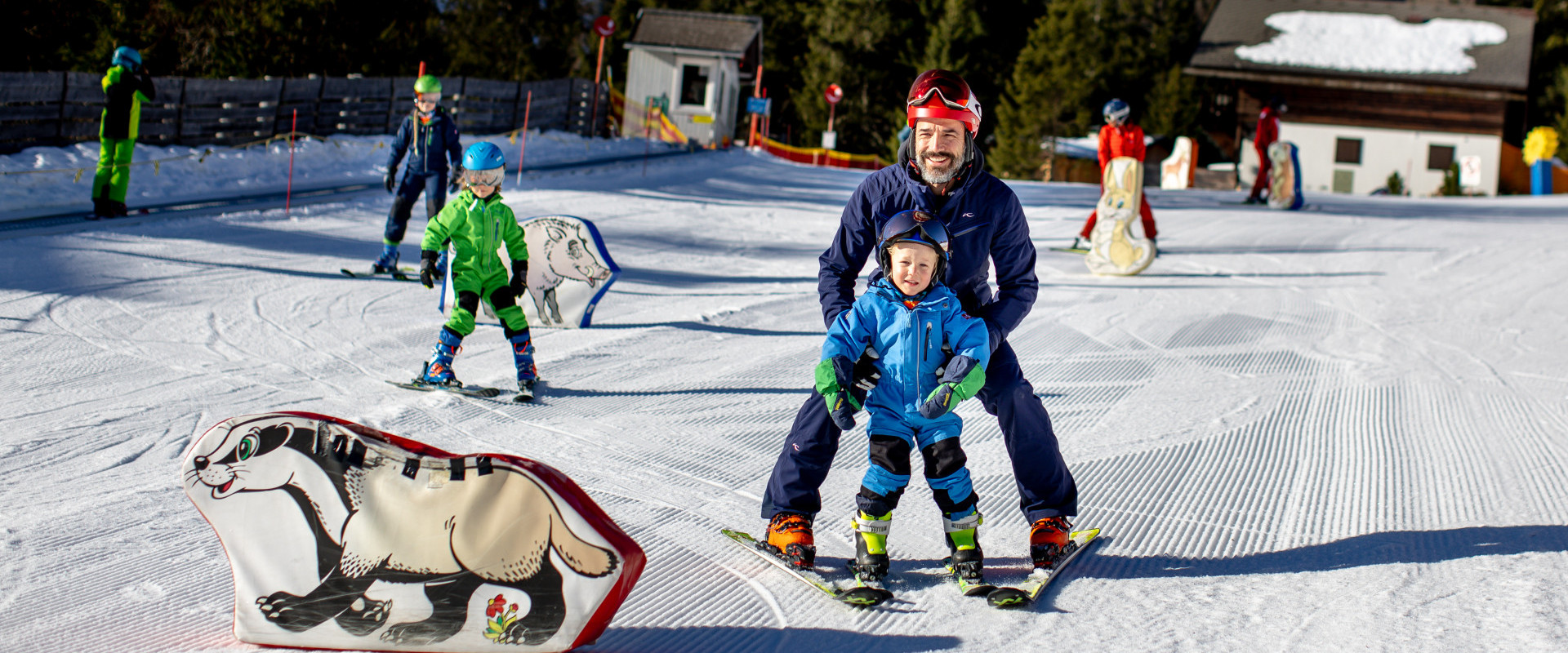 Winter sports scene at Lachtal in Murtal, Styria, Austria, featuring a bustling winter sports centre. Families and individuals, including children learning, are enjoying skiing on the snow-covered slopes.