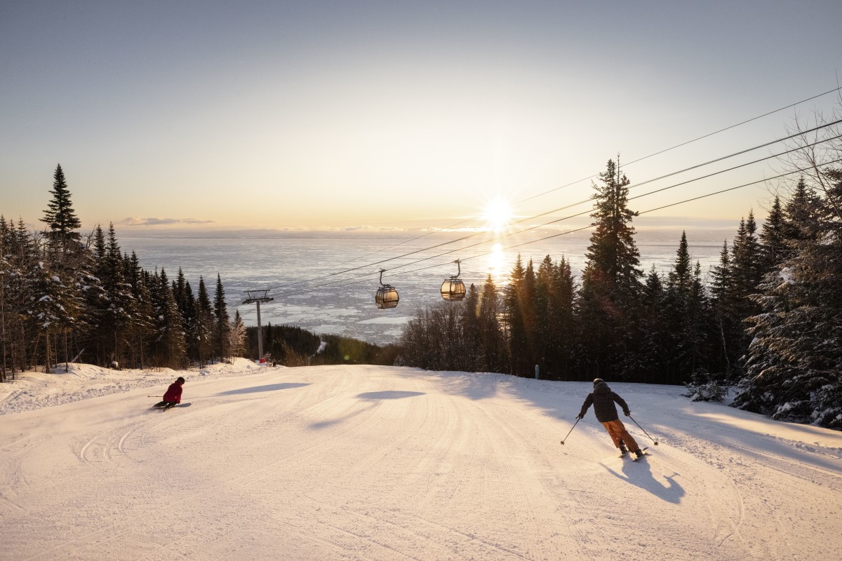 Le Massif de Charlevoix in Canada - two people skiing down a snowy slope at sunset.