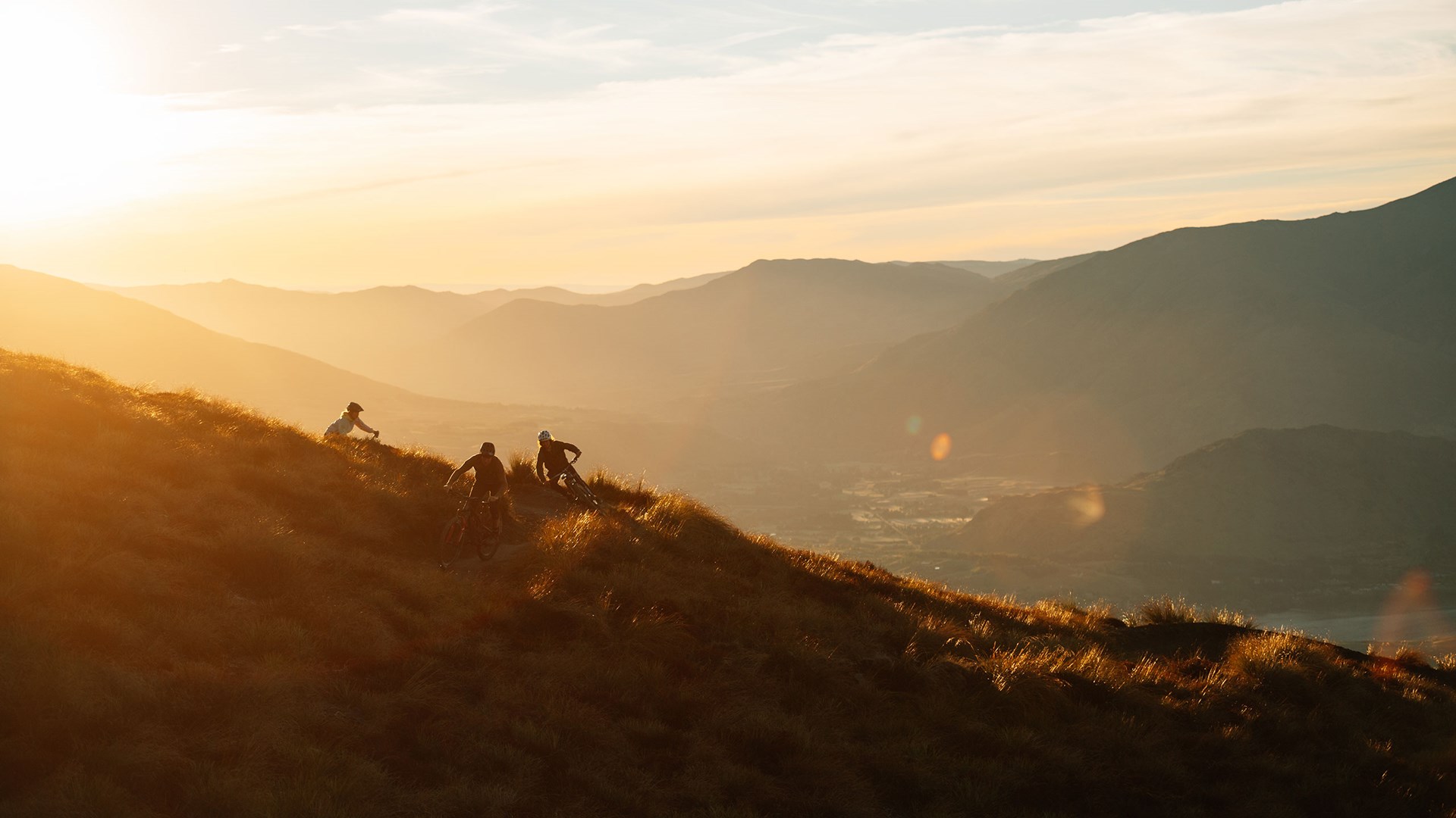 Coronet Peak in New Zealand - two people are hiking up a hill at sunset.