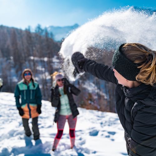 A snowboarder and skier enjoying a winter sports scene at Les Orres ski resort in Gap, France. A family can also be seen skiing in the distance.