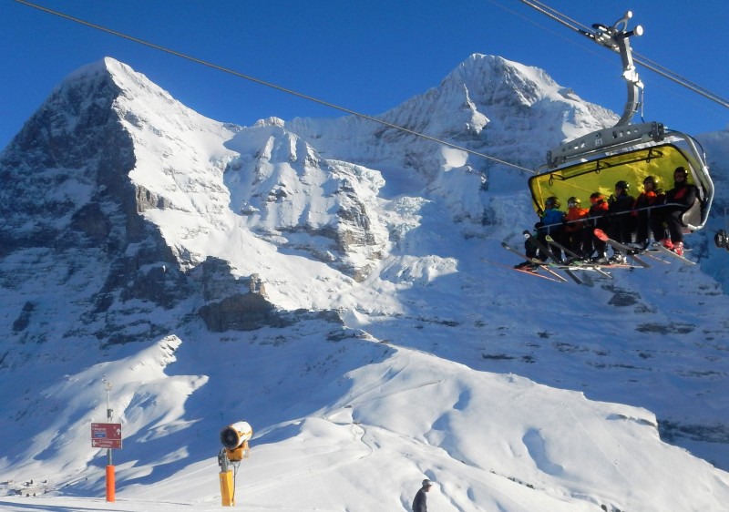 Ski lift ascending a snow-covered slope at Kleine Scheidegg, Grindelwald, Switzerland. Skiers engage in winter sports on the mountain, a chalet nestled nearby.