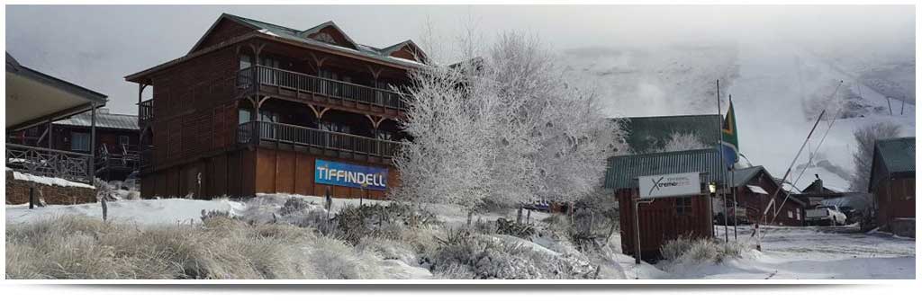 Image showcasing a scenic winter landscape at Tiffindell ski resort in Barkly East, South Africa. A challet is visible amidst the white snow, suggesting an active winter sports scene.