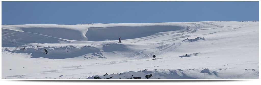 A challet in Tiffindell, South Africa amidst a winter sports scene. A skier and snowboarder are visible on the snowy landscape, partaking in winter activities.
