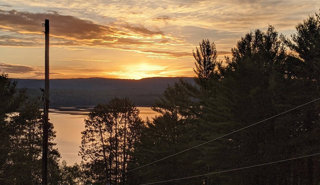 A serene view of Mount Martin in Southern Ontario featuring a calm lake with a charming chalet nestled nearby. Dominating the scene is the majestic mountain under a clear sky. In the distance you can spot a ski lift and a mountain bike nearby.