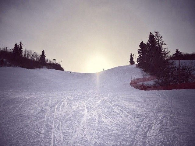A skier on a downhill path at Valley Ski Hill – Alliance in Central Alberta, Canada. The ski resort features a charming chalet, snow-covered slopes and a passing ski lift. Perfect winter sports scene.