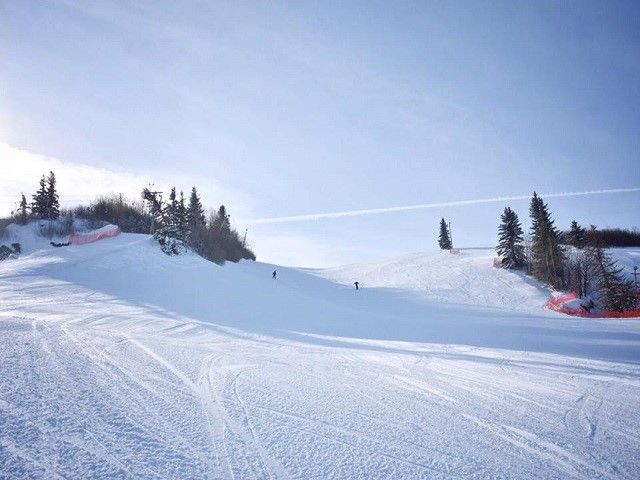 A skier is enjoying a sunny day at Valley Ski Hill - Alliance in Central Alberta, Canada. The winter sports scene is complemented by the scenic ski resort and a charming chalet.