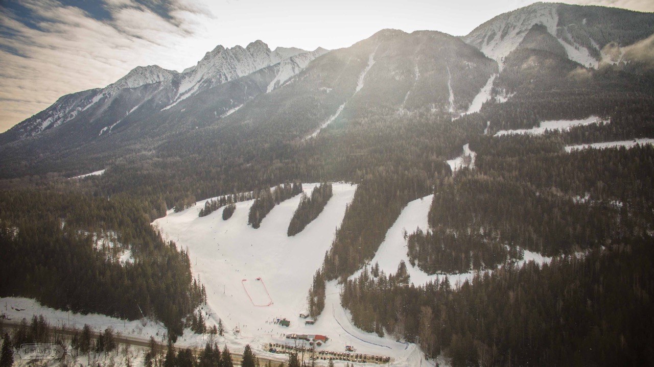 Winter scene of Summit Lake, Nakusp in Kootenay Rockies, British Columbia, with a bustling ski resort and ski lift amid a stunning winter landscape.
