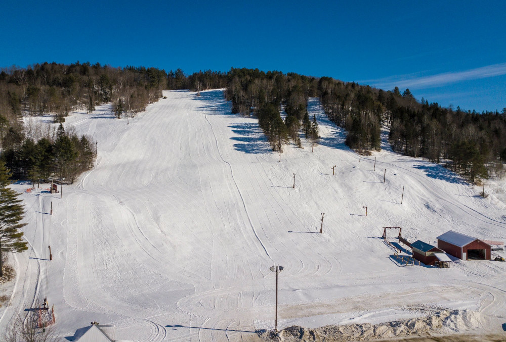Winter scene at Lyndon Outing Club, Vermont, featuring a bustling ski resort with a ski lift heading up the snow-covered slope, and a skier swiftly gliding down.