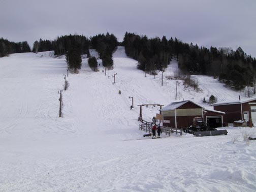 A scenic ski resort at Lyndon Outing Club in Vermont, featuring a quaint challet with a nearby ski lift. The scene is brimming with winter sports enthusiasts, making it a bustling winter sports centre.