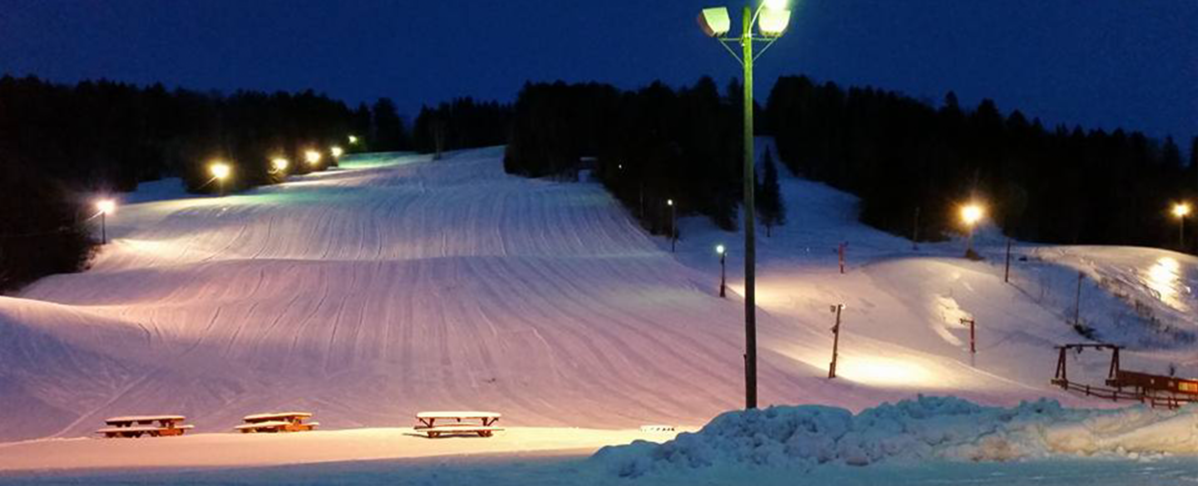 A bustling winter sports scene at Lyndon Outing Club in Vermont featuring a charming chalet a well-equipped winter sports center and a ski resort. A solitary snowmobile trails in the snow-filled landscape.