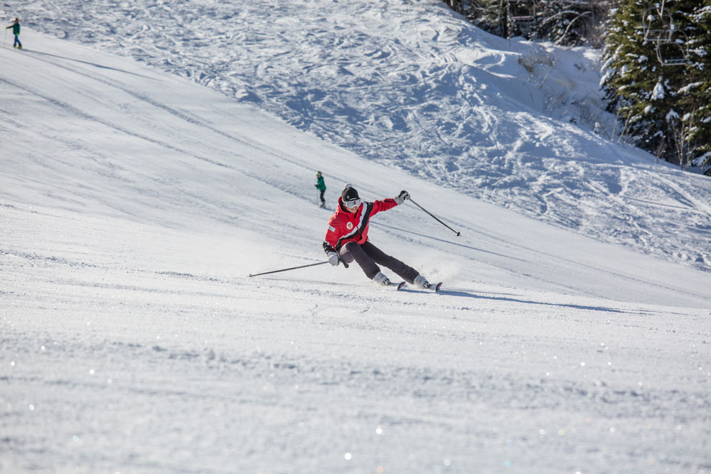 A skier enjoying the snowy slopes at Kolašin 1450 | Kolašin 1600 in Montenegro, with a charming chalet and bustling winter sports centre in the background.