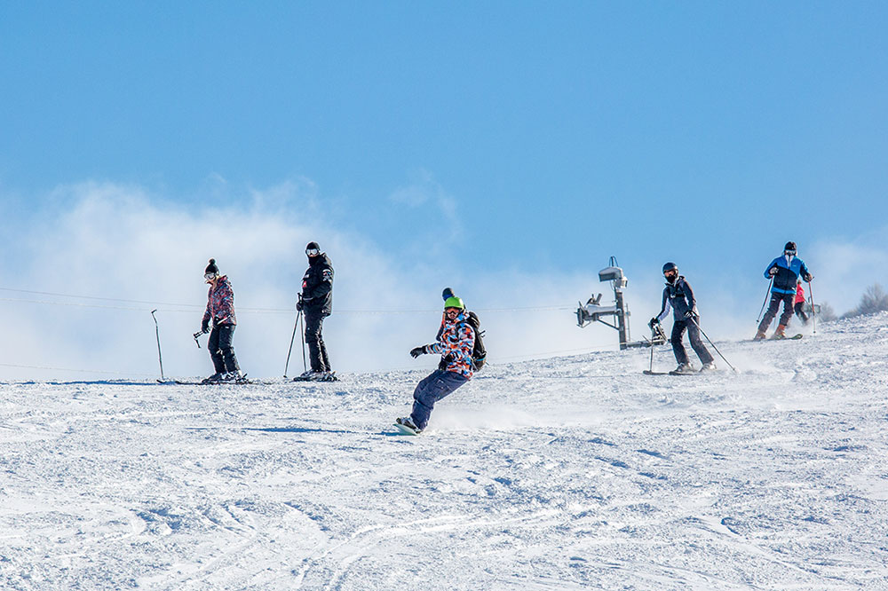 A vibrant winter sports scene at Kolašin in Montenegro, featuring numerous people skiing down the slopes, a ski lift in operation, and a family enjoying their ski adventure.