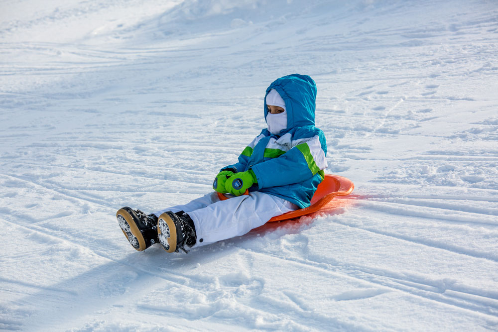 Winter sports action at Kolašin 1450 | Kolašin 1600 in Montenegro featuring a skier and snowboarder in motion, a child learning to ski, against the backdrop of a cozy chalet.