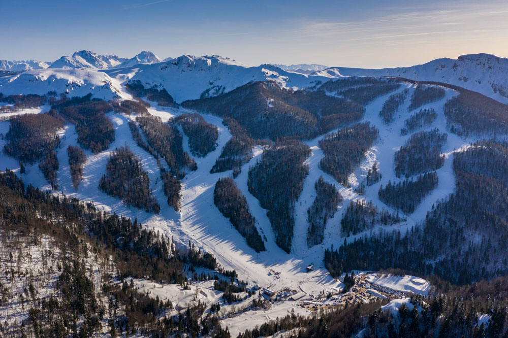 View of the Kolašin ski resort in Montenegro, showcasing snow-covered slopes and a ski lift, with people enjoying winter sports amidst stunning winter scenery.