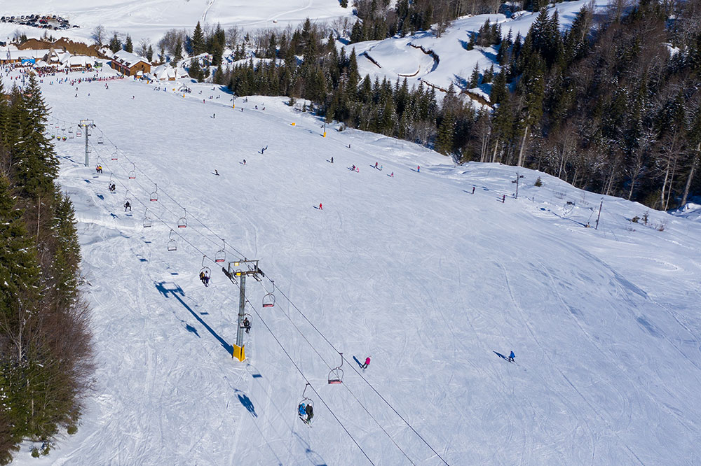 Winter sports scene at Kolašin 1450 | Kolašin 1600 ski resort in Montenegro featuring a ski lift, a skier, and a group of people enjoying the slopes.