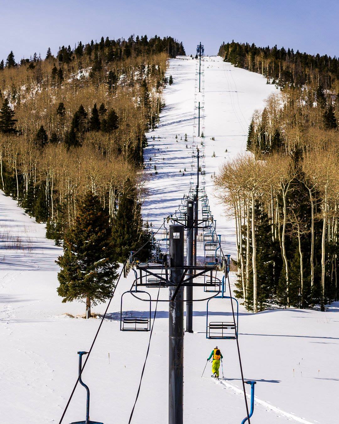 Ski lift ascending a snow-covered slope at Cuchara Mountain Park, a ski resort in Colorado. A skier is making their way down the winter landscape.
