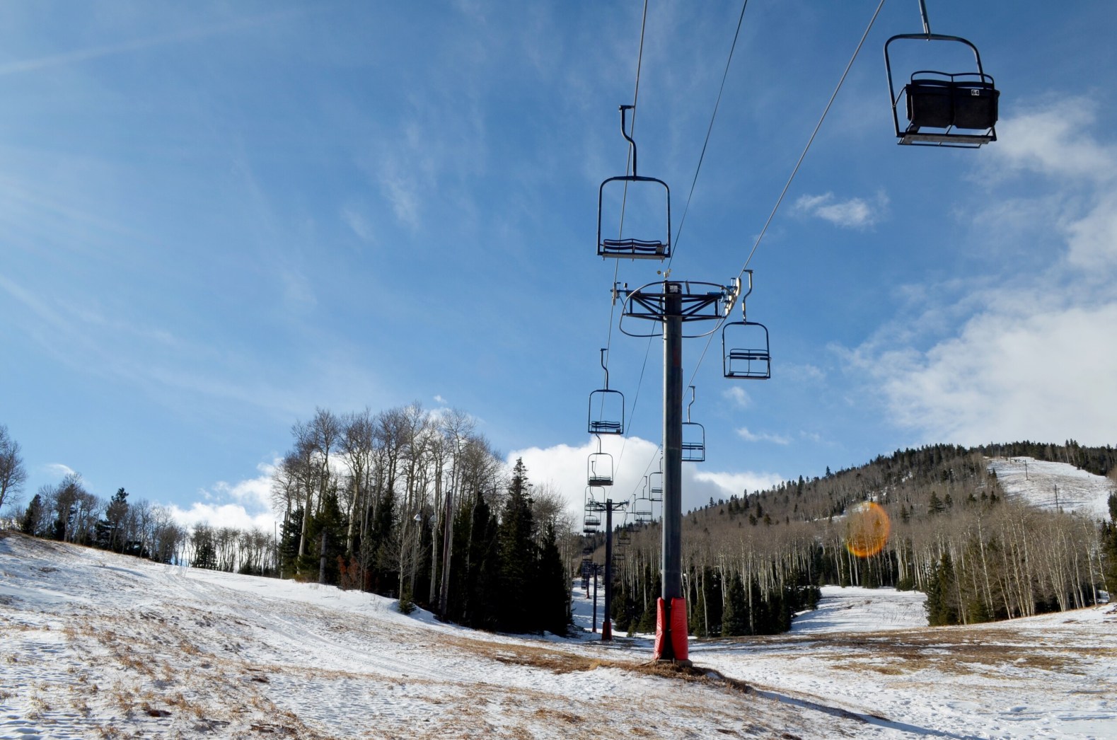 View of Cuchara Mountain Park in Colorado featuring a prominent ski lift against a wintry backdrop. Skiers and a ski resort can be faintly identified in the distance.