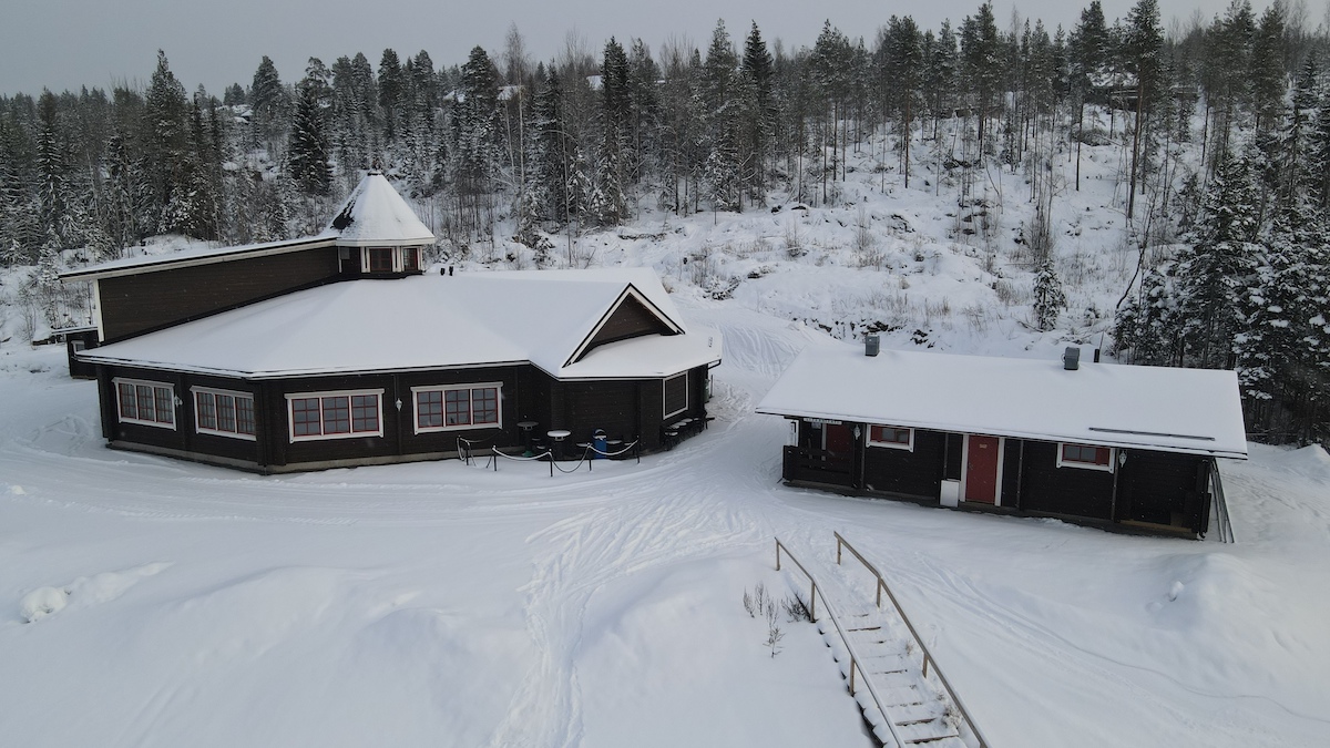 Lakis in Finland - two cabins in the snow with trees in the background.