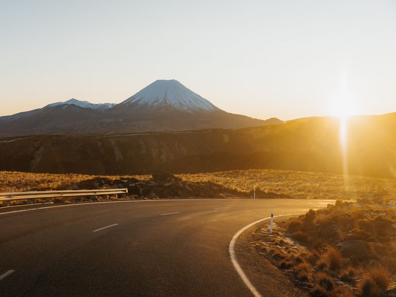 A picturesque view of Mt Ruapehu in Whakapapa, North Island, New Zealand, showcasing a stunning winter landscape with a chalet nestled at the foot of the snow-covered mountain on a sunny day.