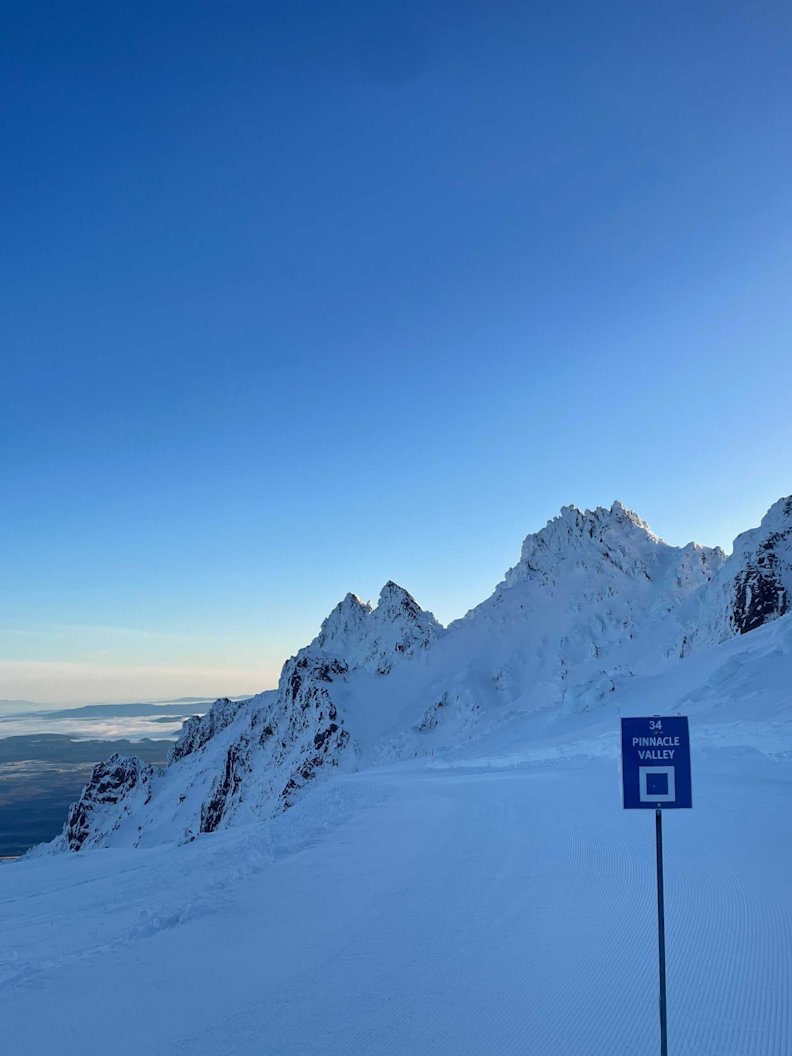 Skiers enjoy a day on the slopes at Whakapapa – Mt Ruapehu in New Zealand, with a picturesque mountain backdrop, a snow-covered ski resort, and a charming chalet nearby.