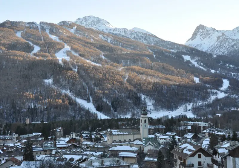 Breathtaking view of Bardonecchia in Turin, Italy showcasing a charming chalet nestled amidst a stunning winter landscape. Snow-covered mountain and a bustling ski resort can also be seen.