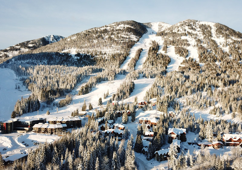View of the bustling Red Mountain Ski Resort in Rossland, British Columbia, with skiers and snowboarders enjoying the snow-covered slopes beneath winter skies.
