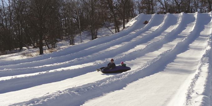 A winter sports scene at Whitetail Ridge in Wisconsin featuring a skier and a snowmobile near a chalet part of a winter sports centre.
