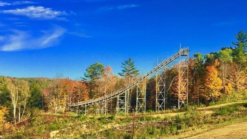 View of Storrs Hill in Lebanon, New Hampshire, highlighting a ski lift rising up the snow-covered mountain. A small chalet and the sprawling ski resort can be seen amidst the winter sports scene.