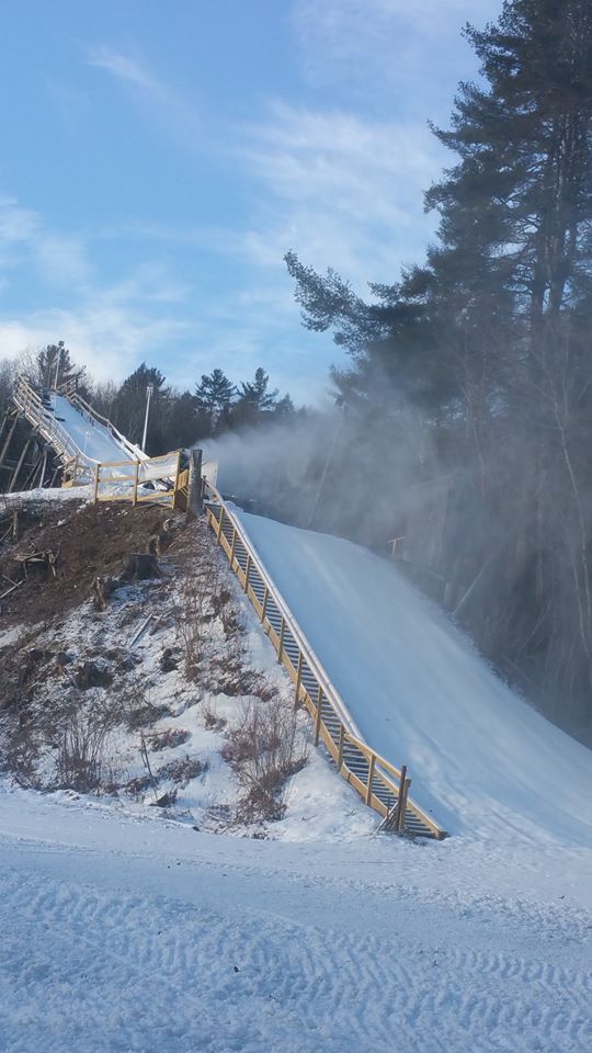 Winter sports enthusiasts enjoying the snowy slopes at Storrs Hill Ski Resort in Lebanon, New Hampshire, with a cozy chalet in the backdrop amidst beautiful winter scenery.