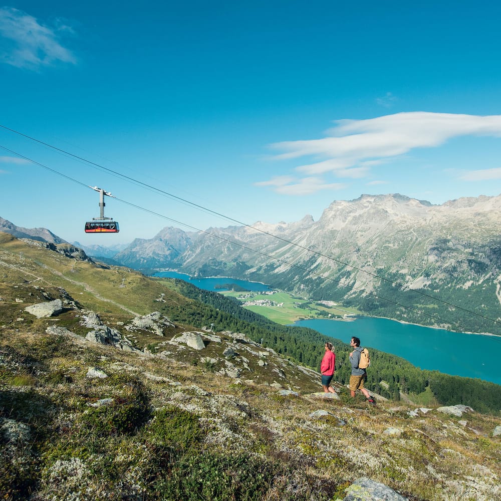 Zuoz – Pizzet | Albanas in Switzerland - two people walking up a mountain with a view of a lake.